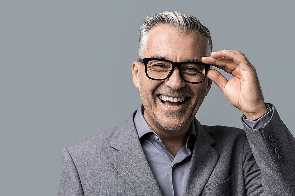 ein lachender Mann fasst an seine Brille ein lachender Mann fasst an seine Brille