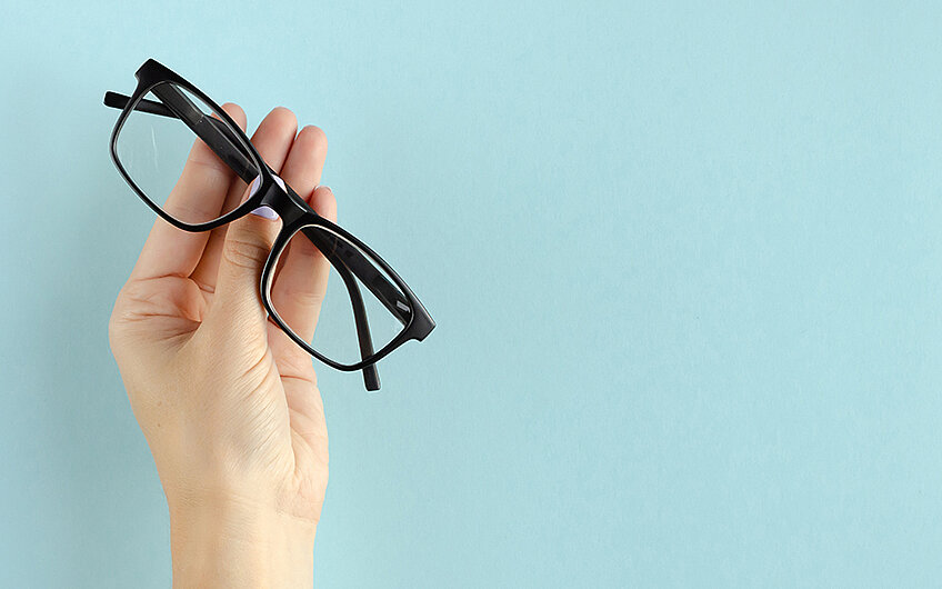 ein lachender Mann fasst an seine Brille eine Hand hält eine Brille
